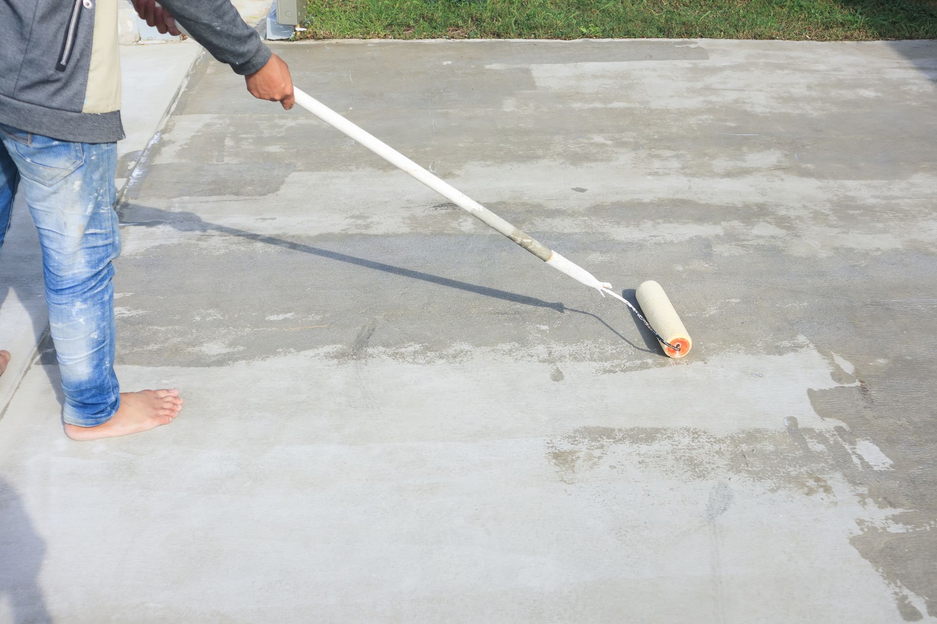A man is painting a concrete driveway with a roller.