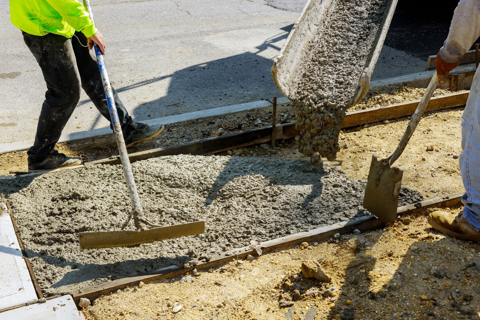 A man is spreading concrete on a sidewalk with a shovel and rake.