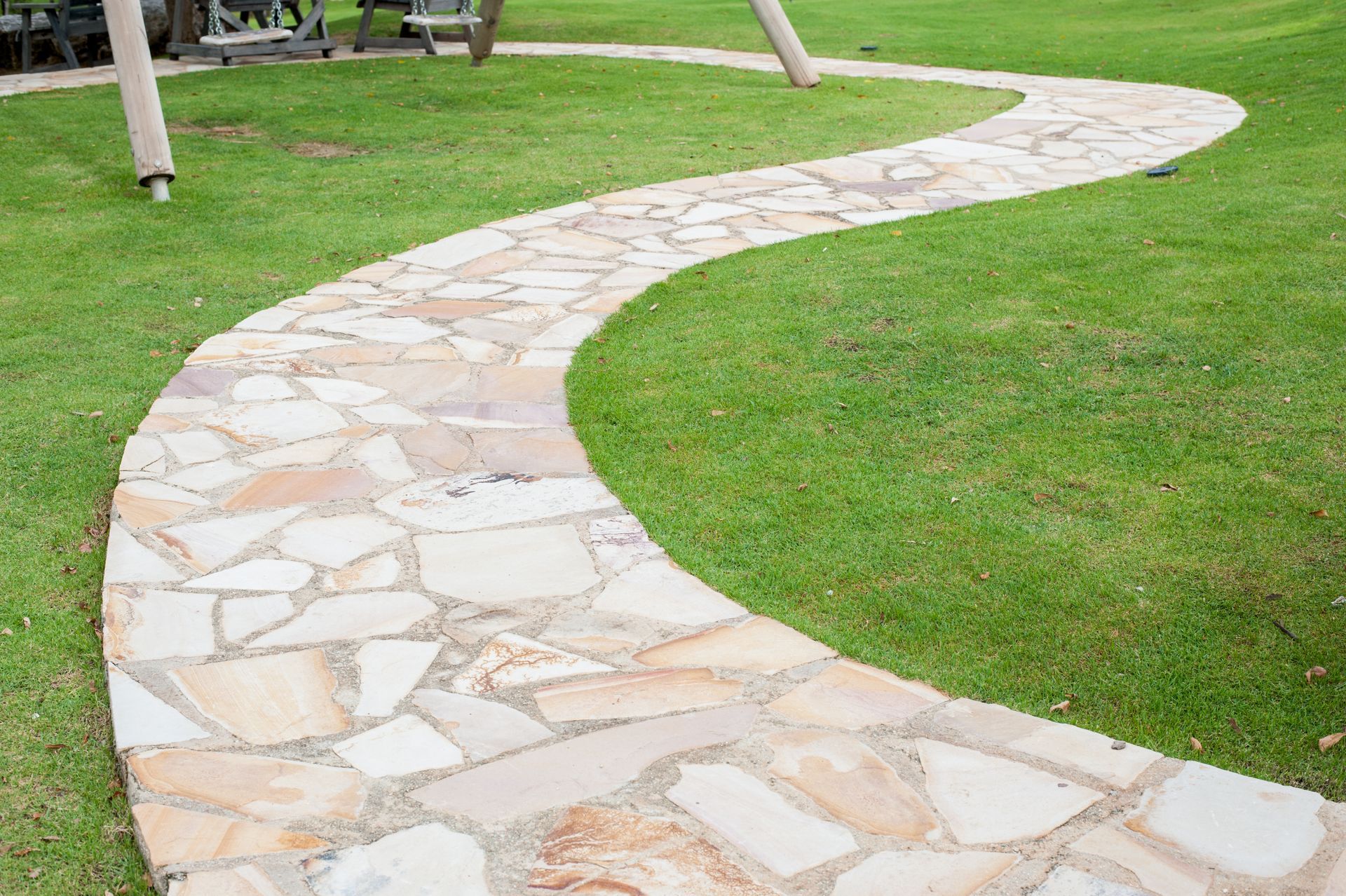 A stone walkway in a park with a swing set in the background.