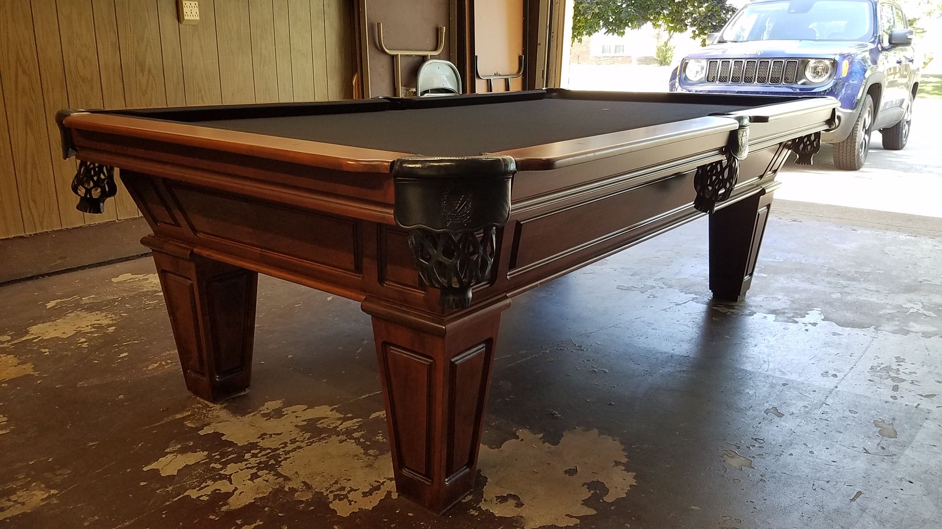 A pool table is sitting in a garage next to a blue truck.