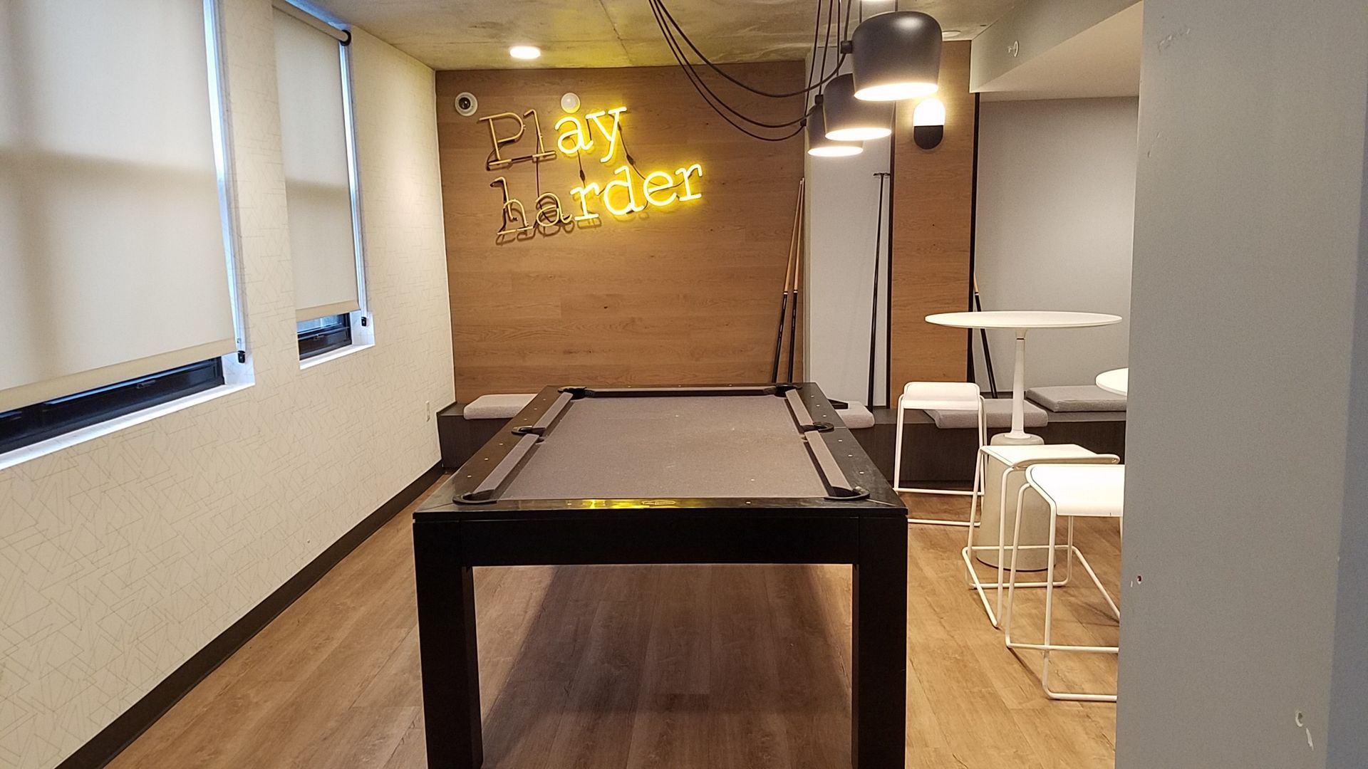 A pool table in a room with a neon sign that says play harder