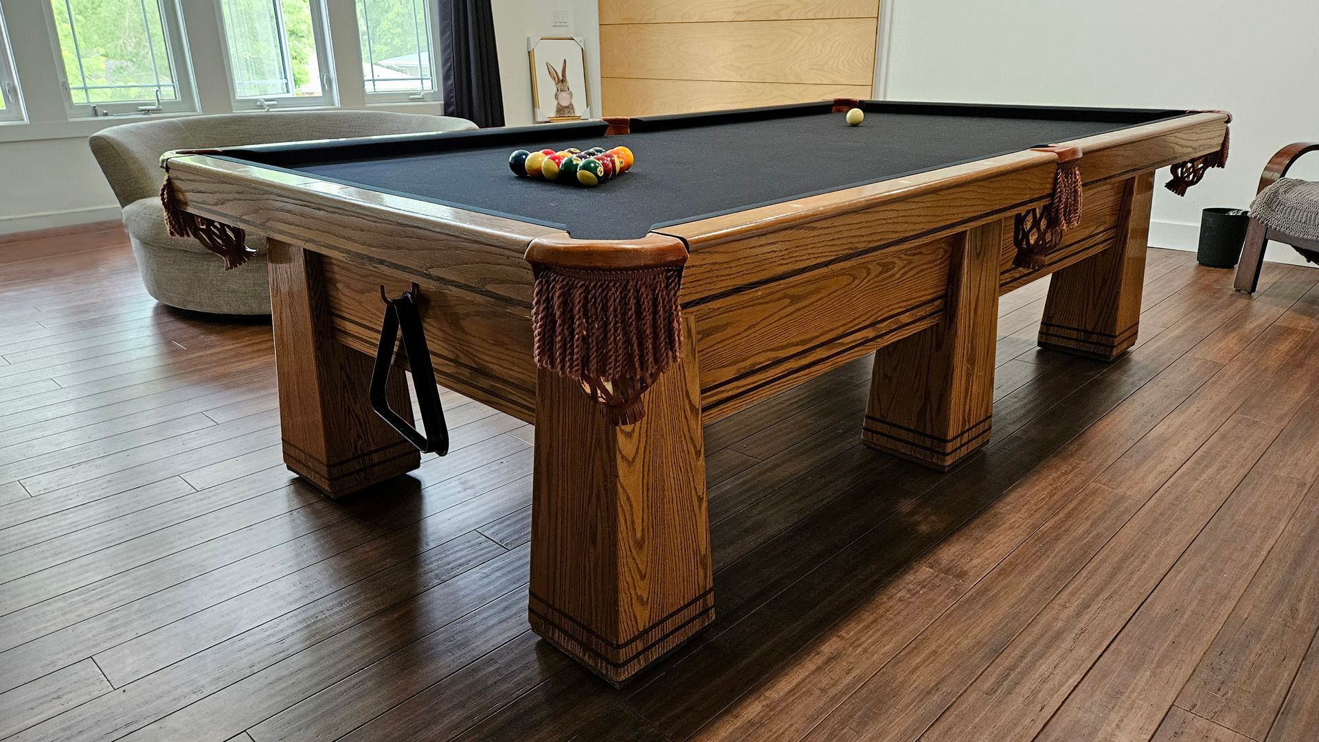 Wooden pool table with balls, set in a room with hardwood floors, and windows.