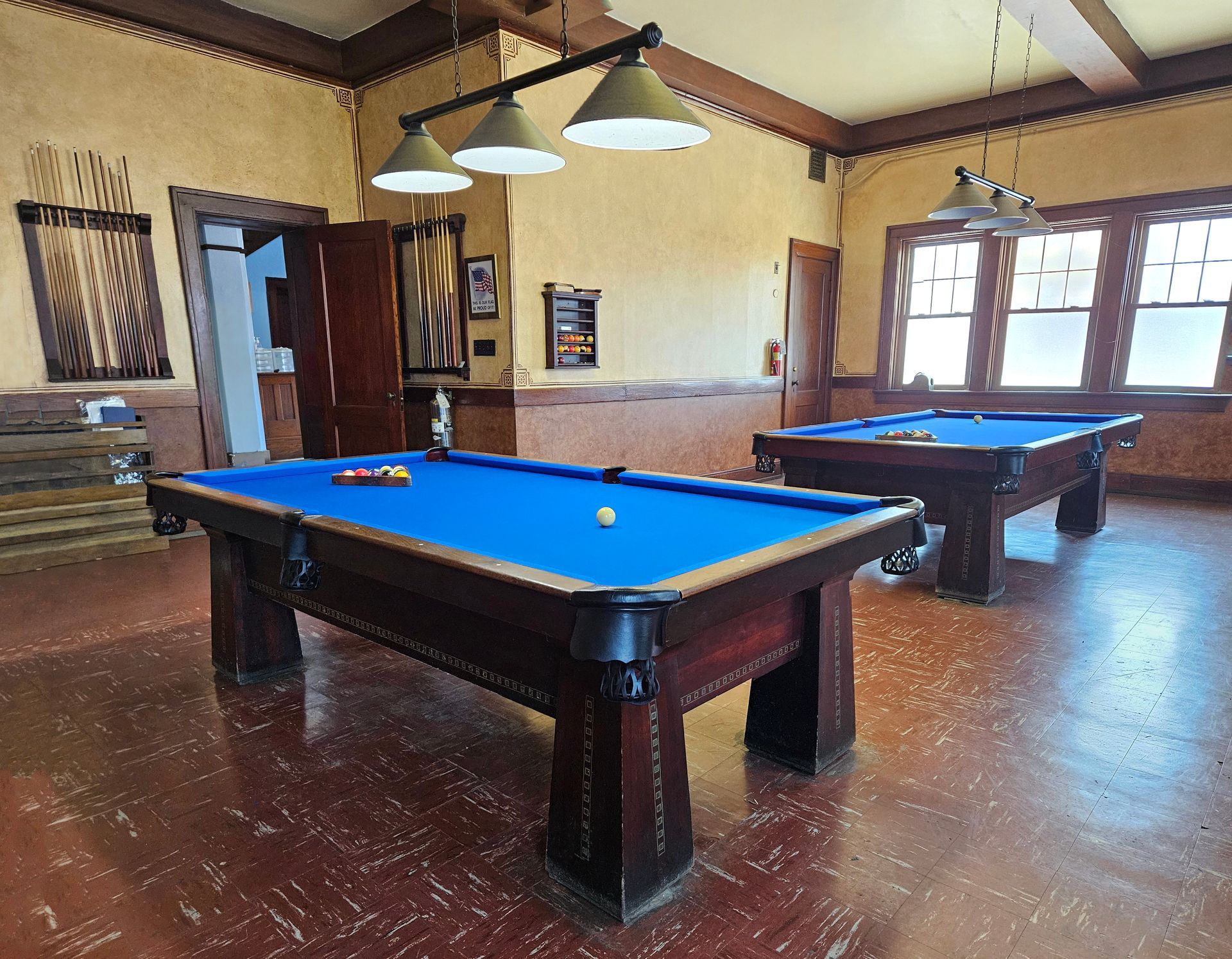 Two pool tables with blue felt in a room with brown and tan walls, and hardwood floors.