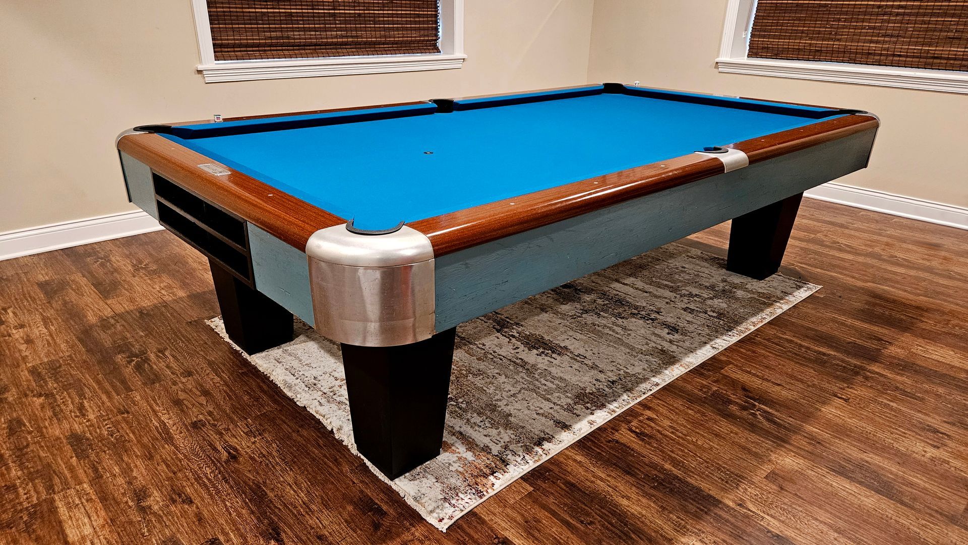 A pool table with a blue cloth is sitting on a rug in a room.