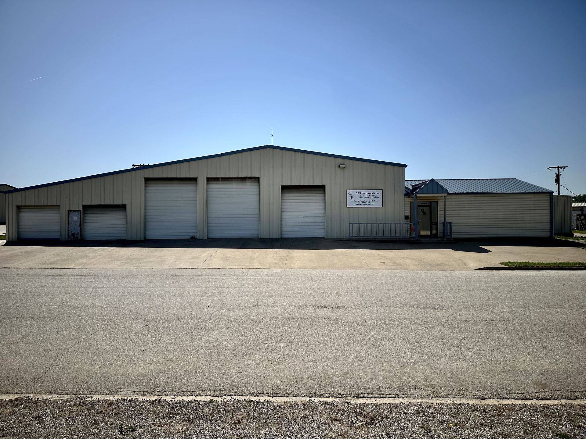 Tan industrial building with three garage doors, a small office entrance, and a blue roof on a sunny day.
