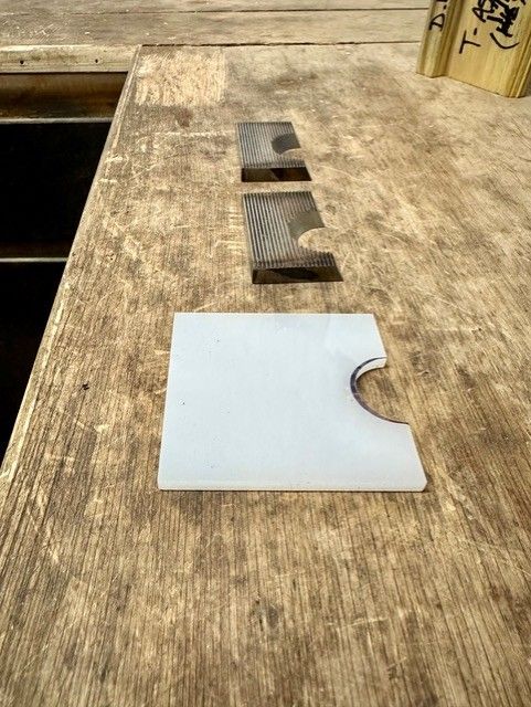 Three wooden pieces on a wooden surface. One white square with a curved cut, and two rectangular pieces.