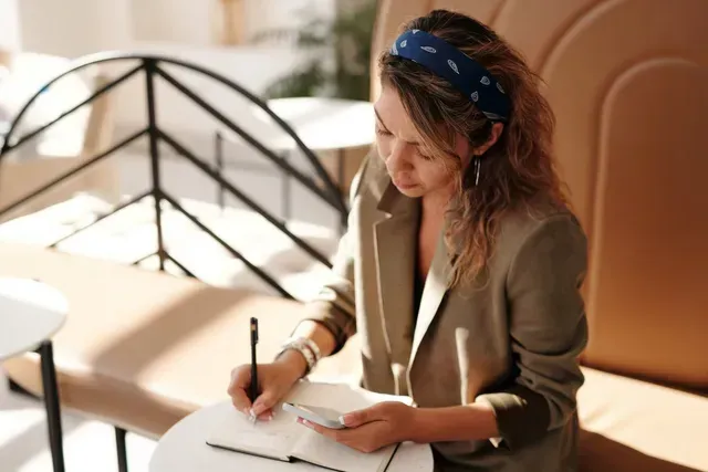 A woman is sitting at a table writing in a notebook.