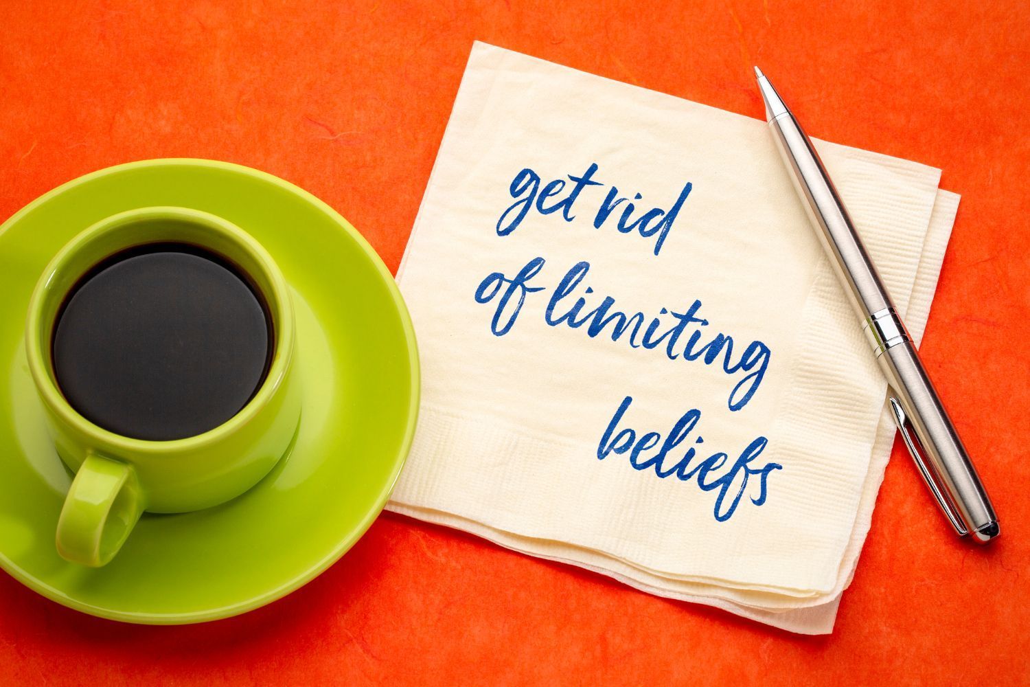 A napkin with the words get rid of limiting beliefs written on it next to a cup of coffee