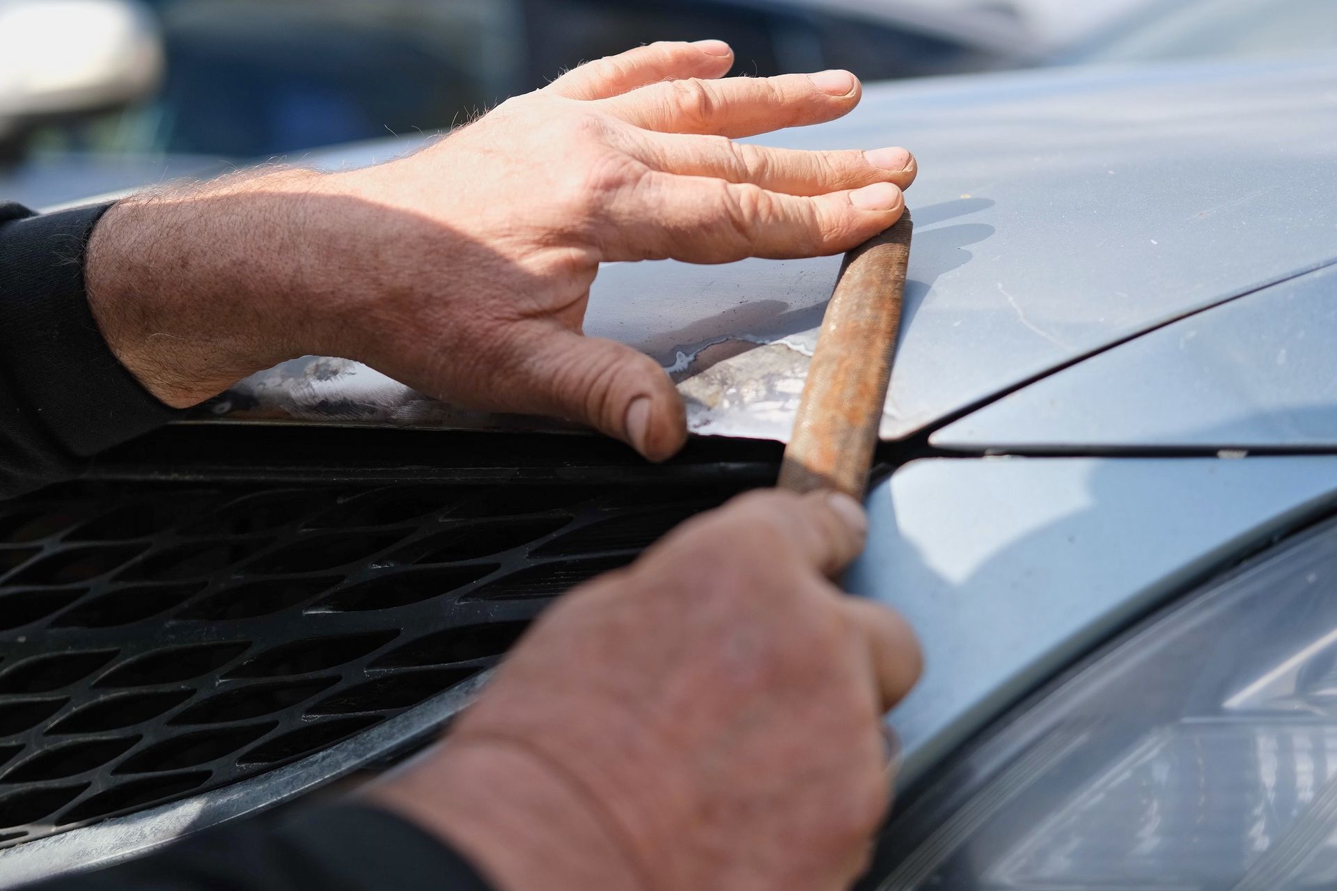 Hands Holding a Wooden Tool Against a Car Hood — Mid Coast Smash Repairs In Forster, NSW