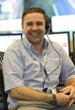 A man wearing a headset is smiling while sitting in front of a computer.