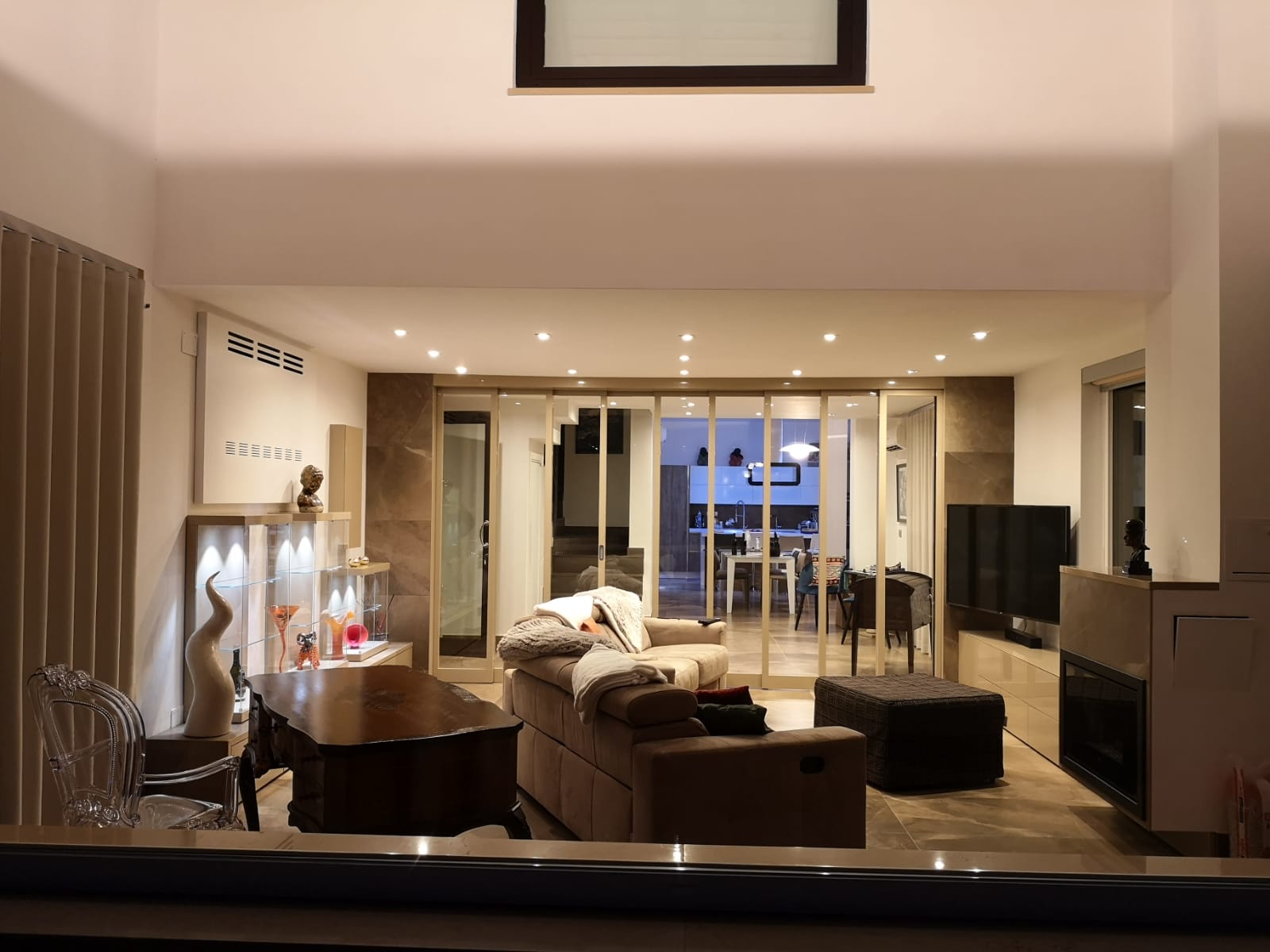 Soggiorno con porte a vetri pieghevoli, sala da pranzo visibile oltre; colori tenui, illuminazione calda.