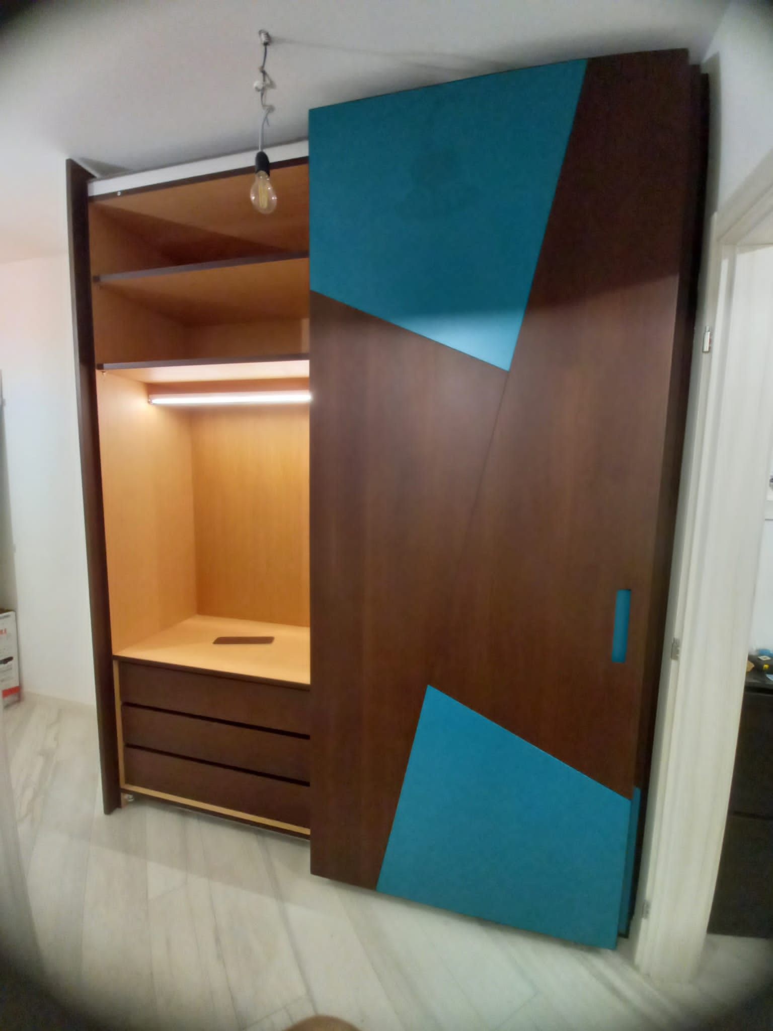 Armadio in legno con dettagli geometrici turchesi; porta scorrevole aperta.