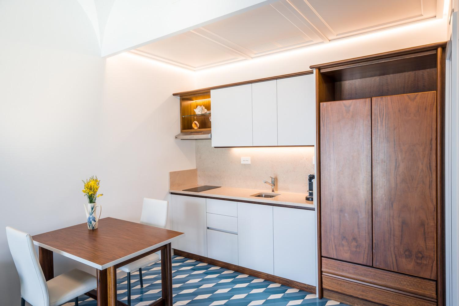 Piccola cucina moderna con mobili bianchi, dettagli in legno e un piccolo tavolo da pranzo.