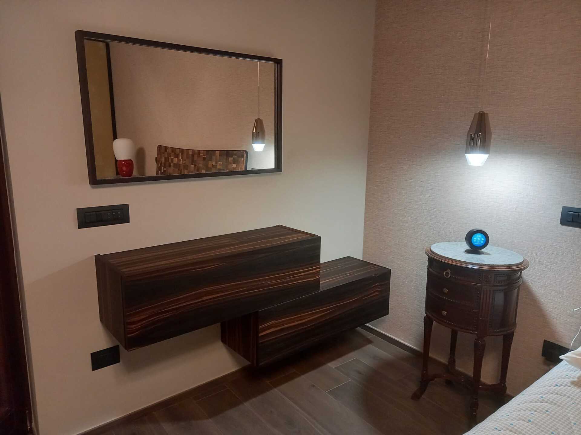 Angolo della camera da letto con moderna cassettiera sospesa, specchio e comodino vintage. Calde tonalità del legno e illuminazione d'atmosfera.