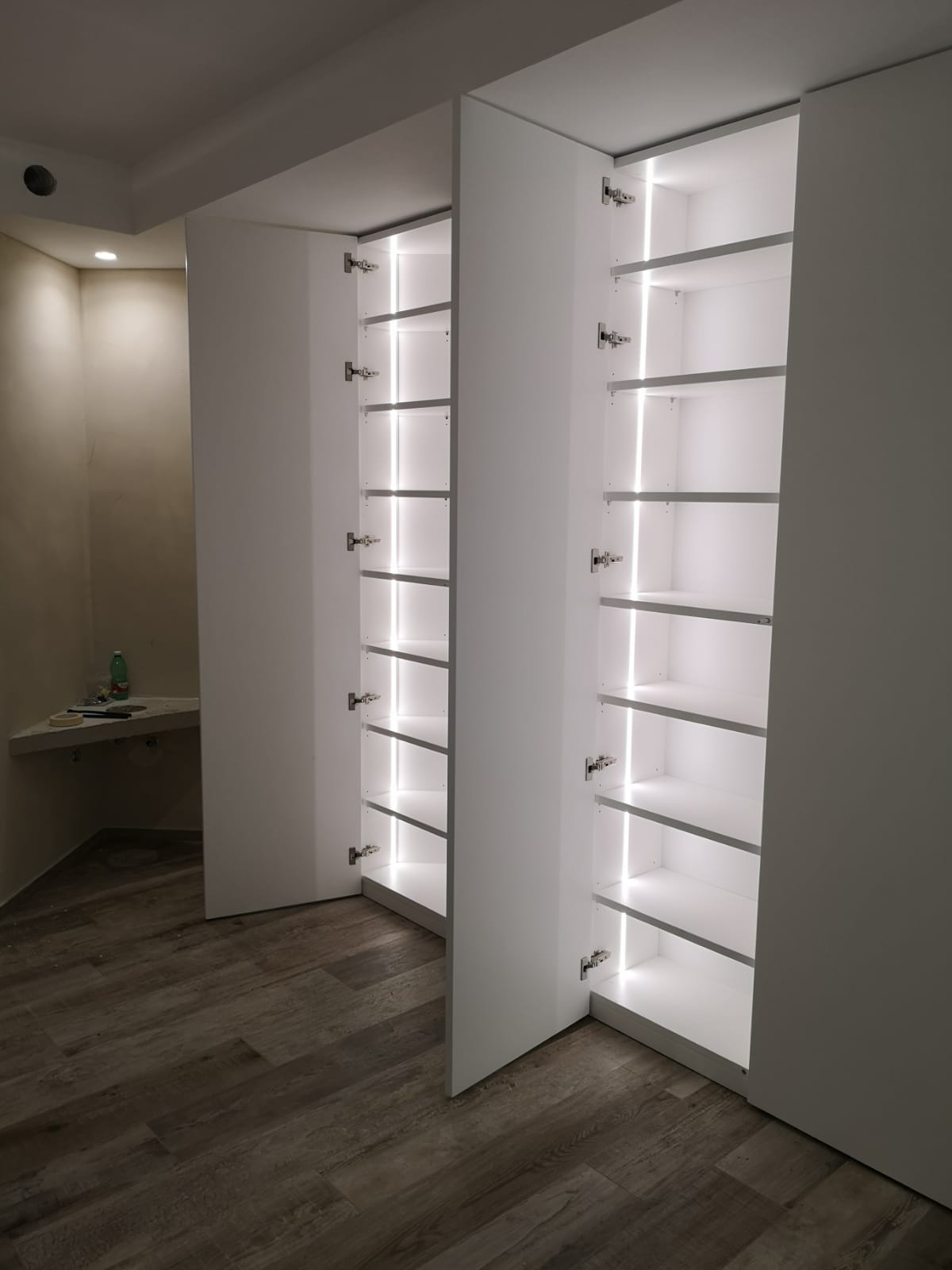 Due mobili contenitori bianchi illuminati con ripiani in una stanza con pavimento in legno.
