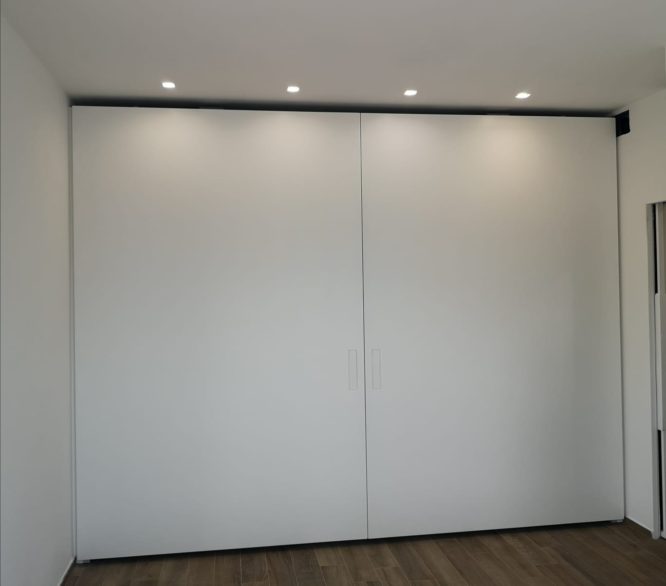 Due grandi porte scorrevoli bianche in una stanza, con luci da incasso nel soffitto e pavimento in legno.