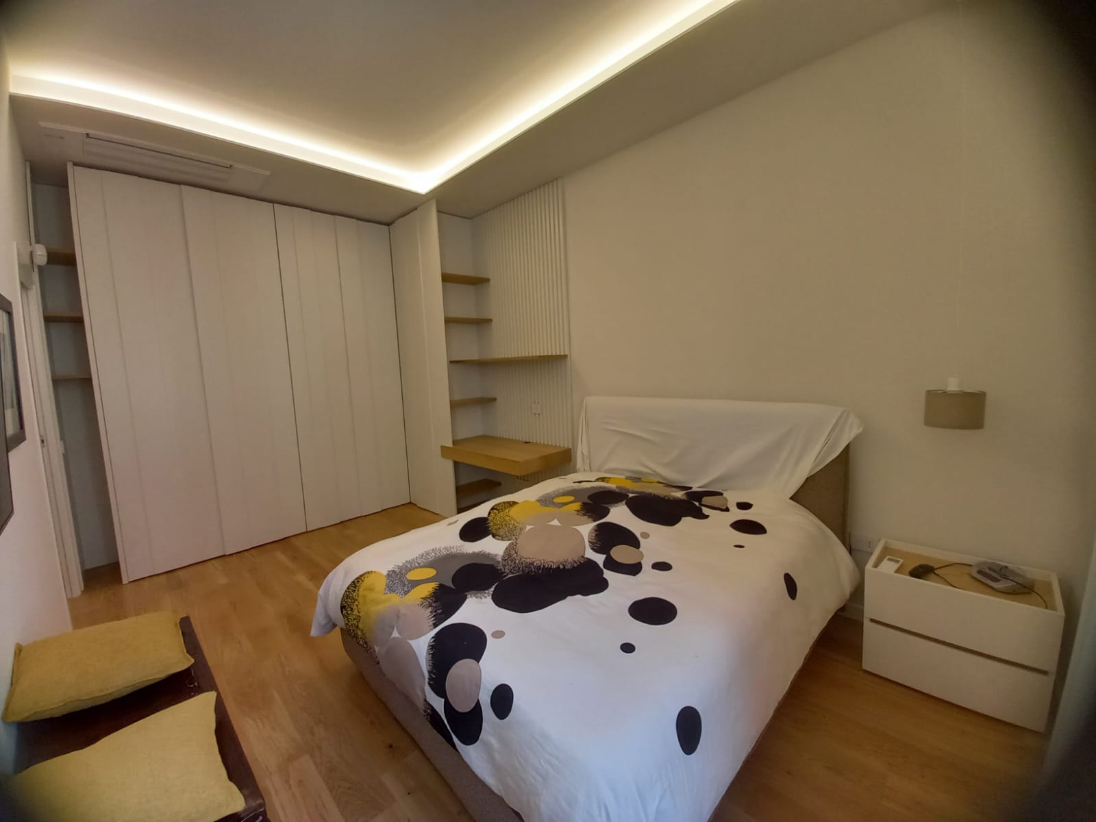 Camera da letto con letto, armadio bianco, pavimento in legno e un tavolino con ripiani.