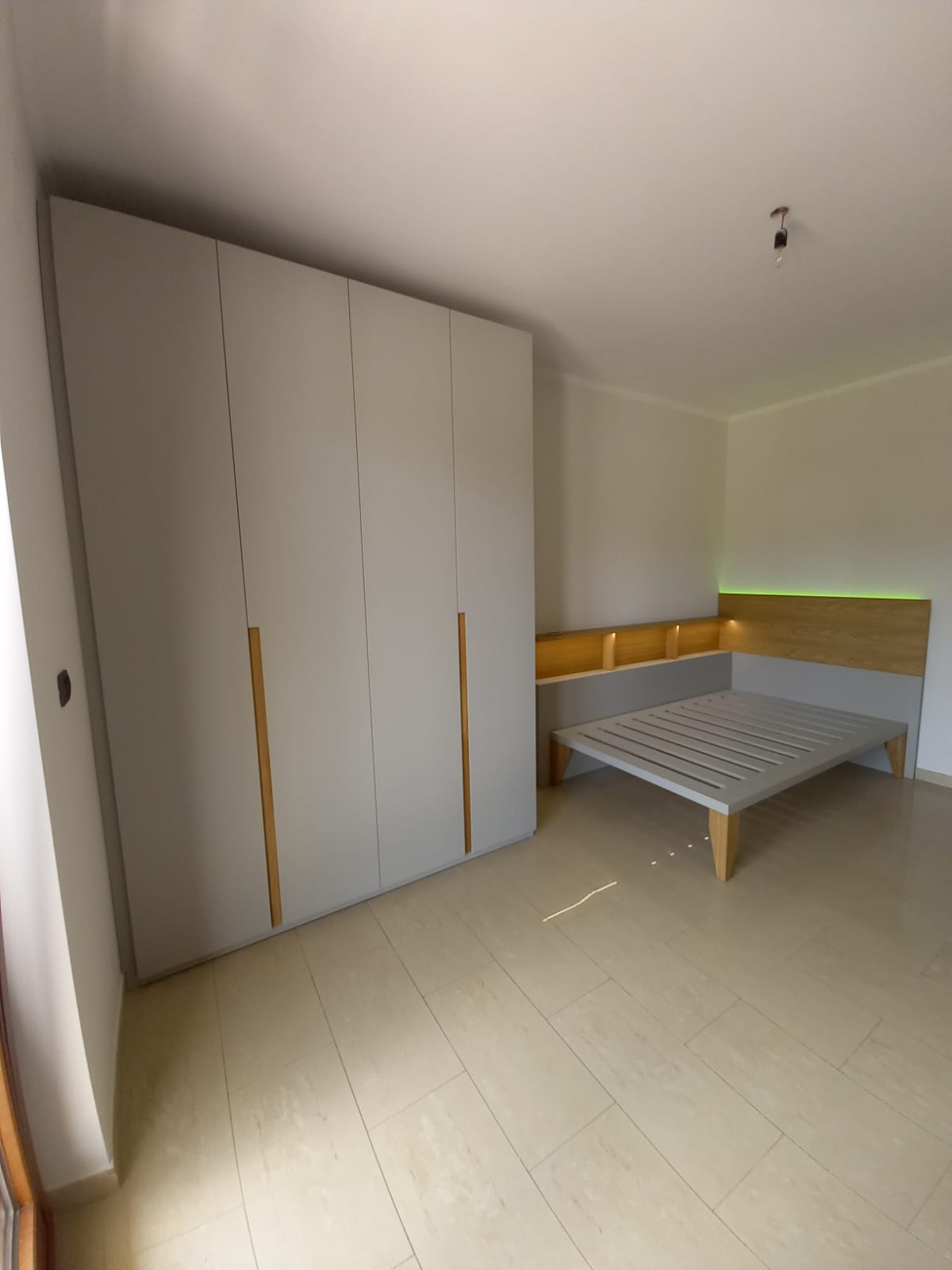 Camera da letto con armadio grigio, letto con testiera in legno e pavimento chiaro.