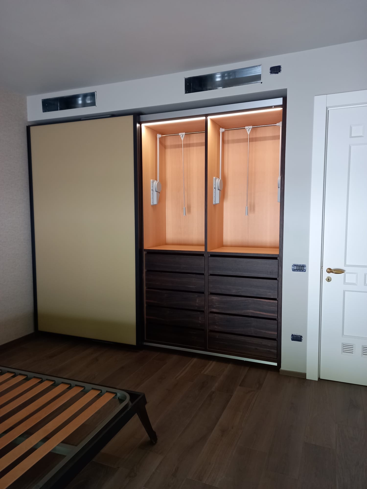 Armadio beige e in legno scuro con anta scorrevole, luci integrate e cassetti, accanto a un'anta bianca.