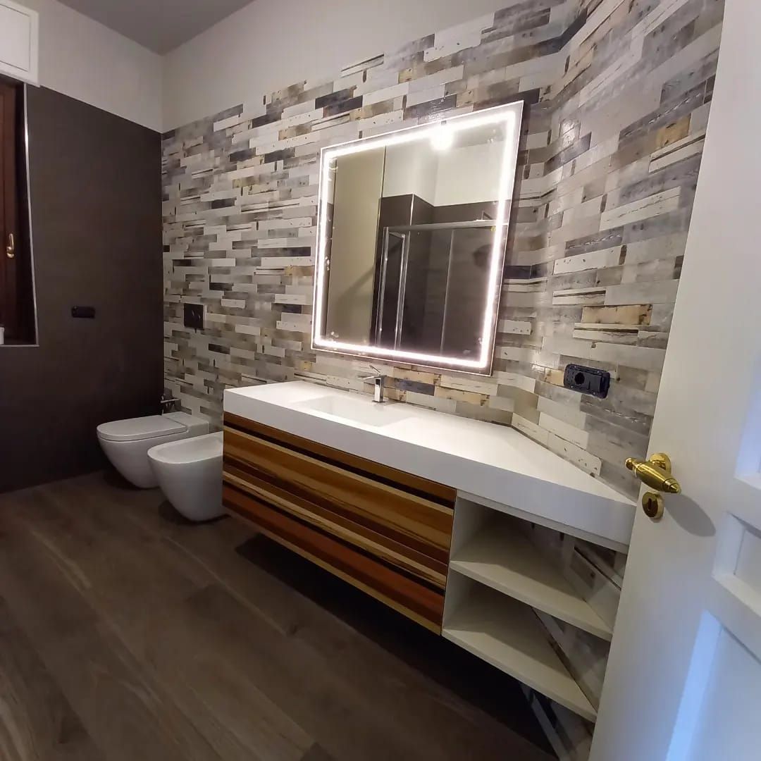 Bagno moderno con parete in pietra, mobile lavabo sospeso e grande specchio illuminato.