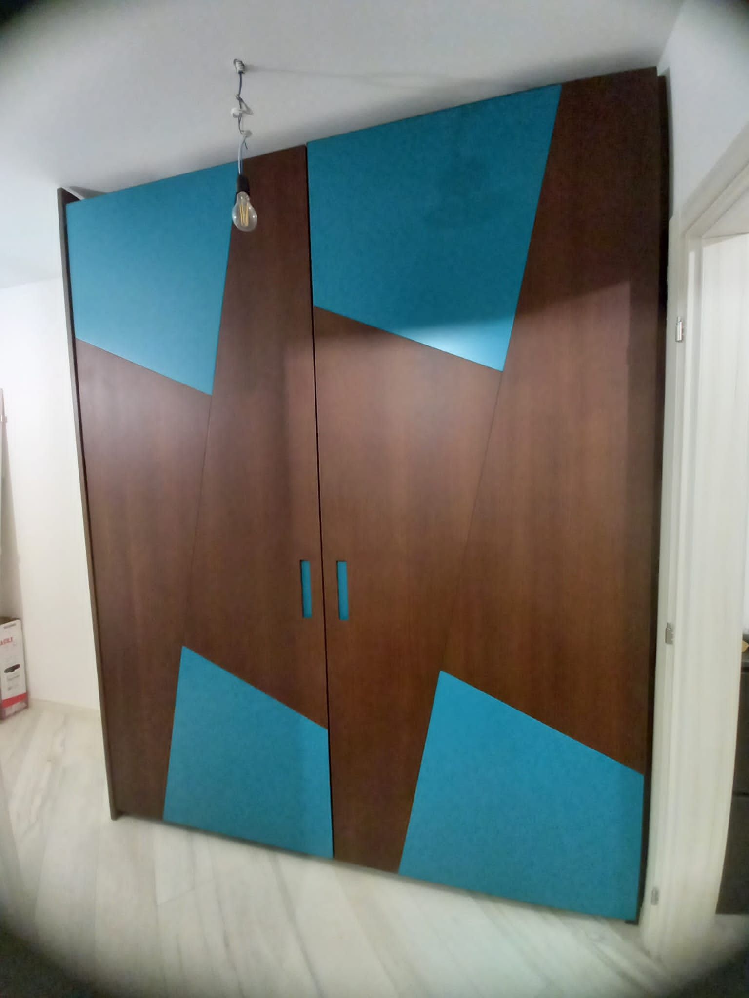 Ampio armadio moderno con ante in legno marrone e dettagli geometrici color verde acqua. In una stanza con pavimento chiaro e lampada a sospensione.