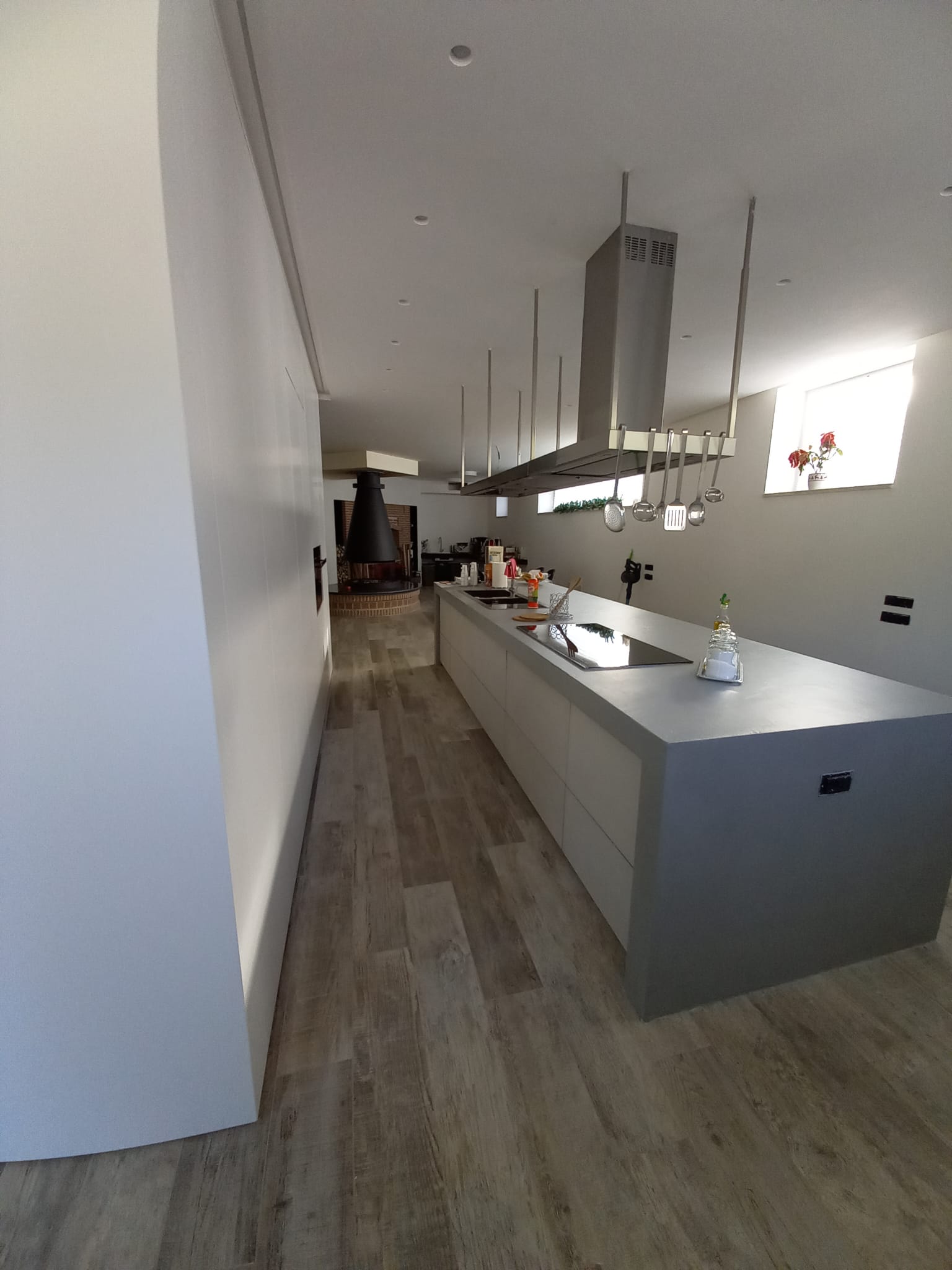 Cucina moderna con grande isola, cappa in acciaio inox, pavimento in legno, pareti bianche.