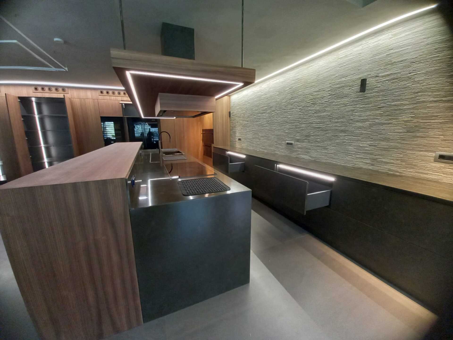 Cucina moderna con mobili in legno e grigio scuro, illuminazione da incasso e parete in pietra.