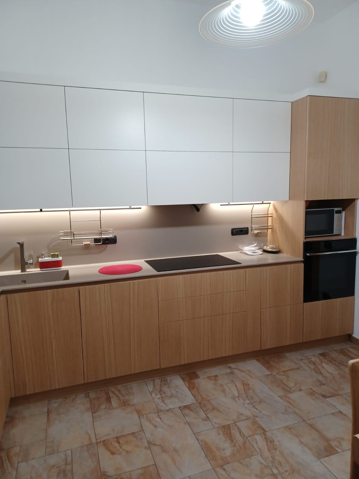 Cucina moderna con mobili in legno chiaro e bianchi, illuminazione da incasso ed elettrodomestici da incasso.