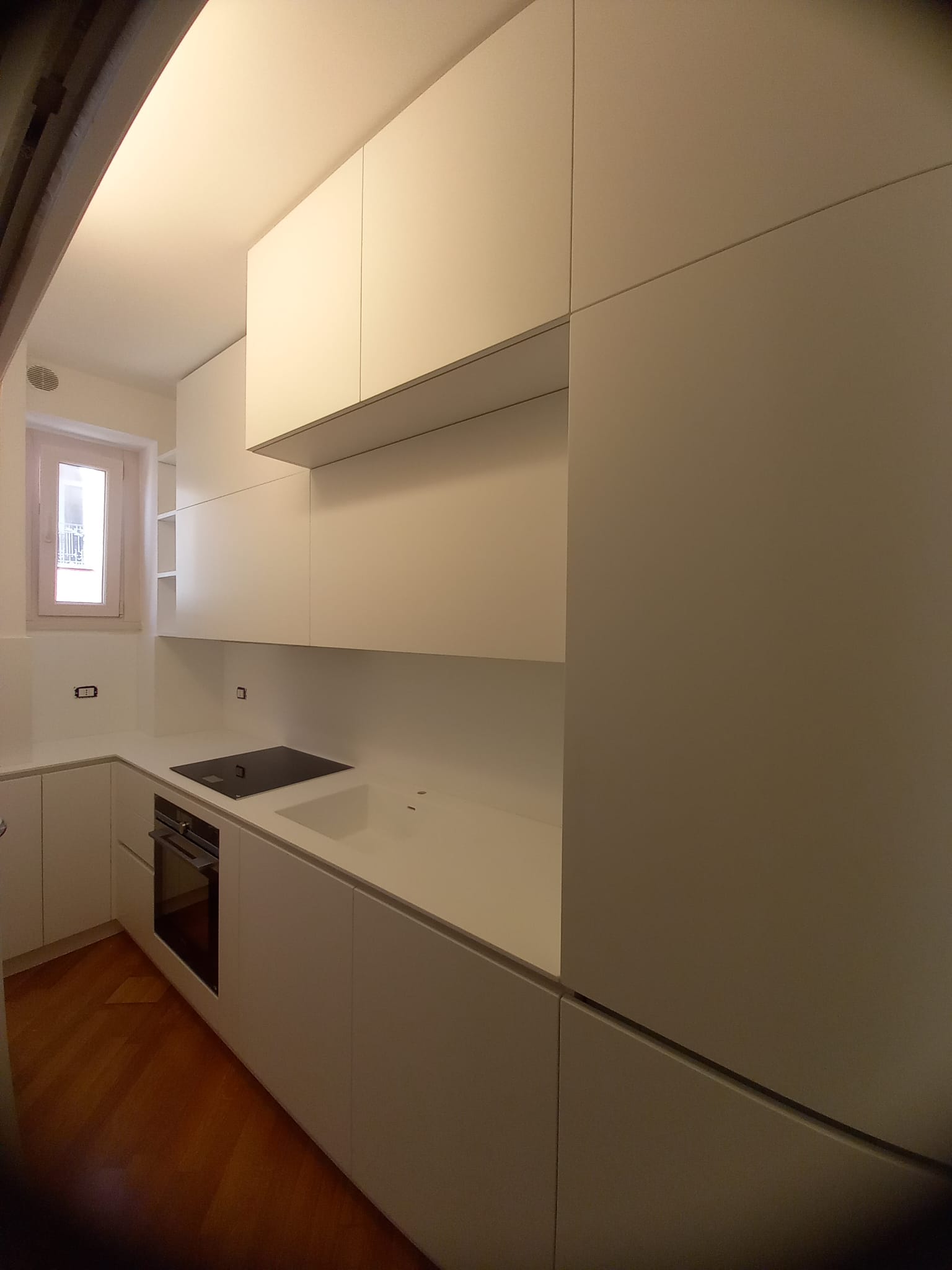 Moderna cucina bianca con pavimenti in legno. Forno e piano cottura integrati. Piccola finestra sulla sinistra.