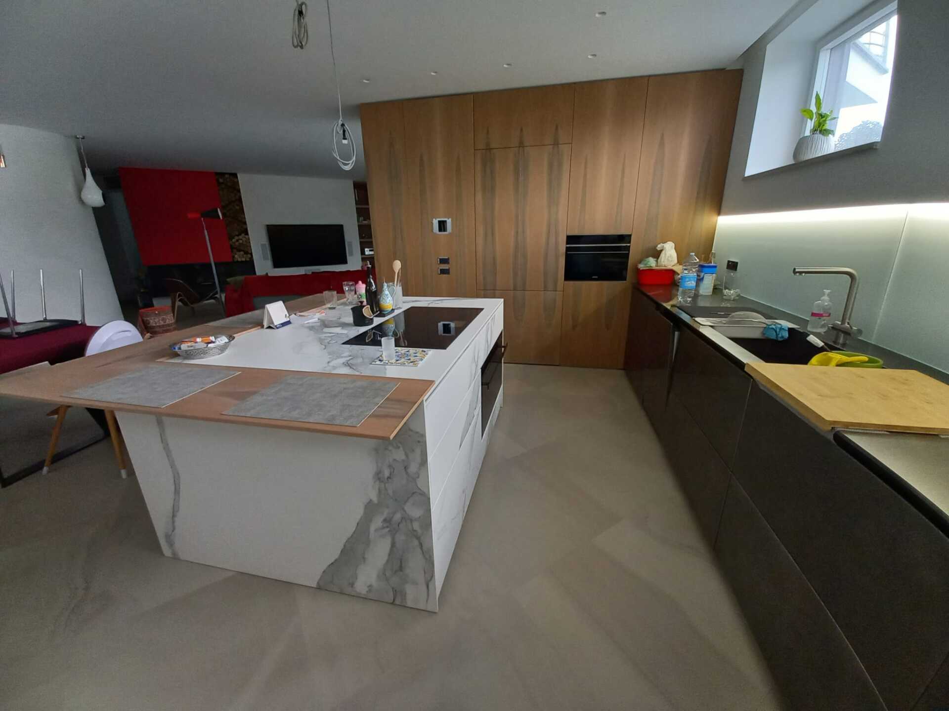 Cucina moderna con isola in marmo, mobili in legno e piano di lavoro scuro.