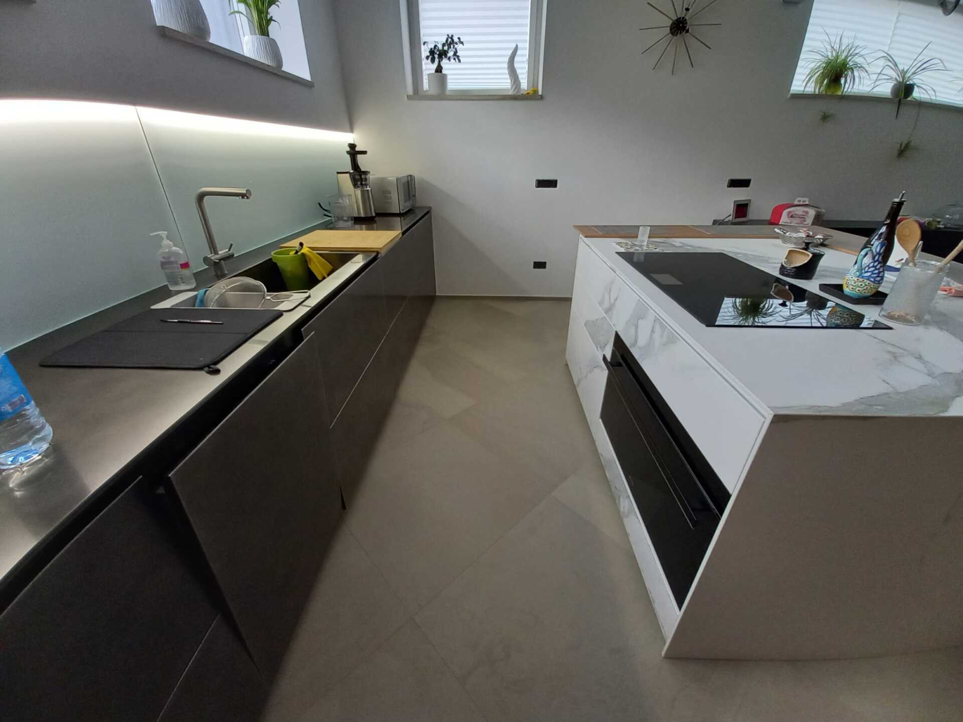 Cucina moderna con mobili grigi, isola in marmo, lavello in acciaio inossidabile.