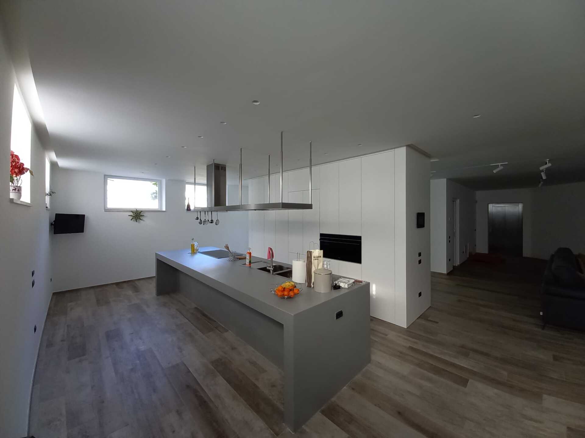 Cucina moderna con isola grigia, mobili bianchi e pavimenti in legno.