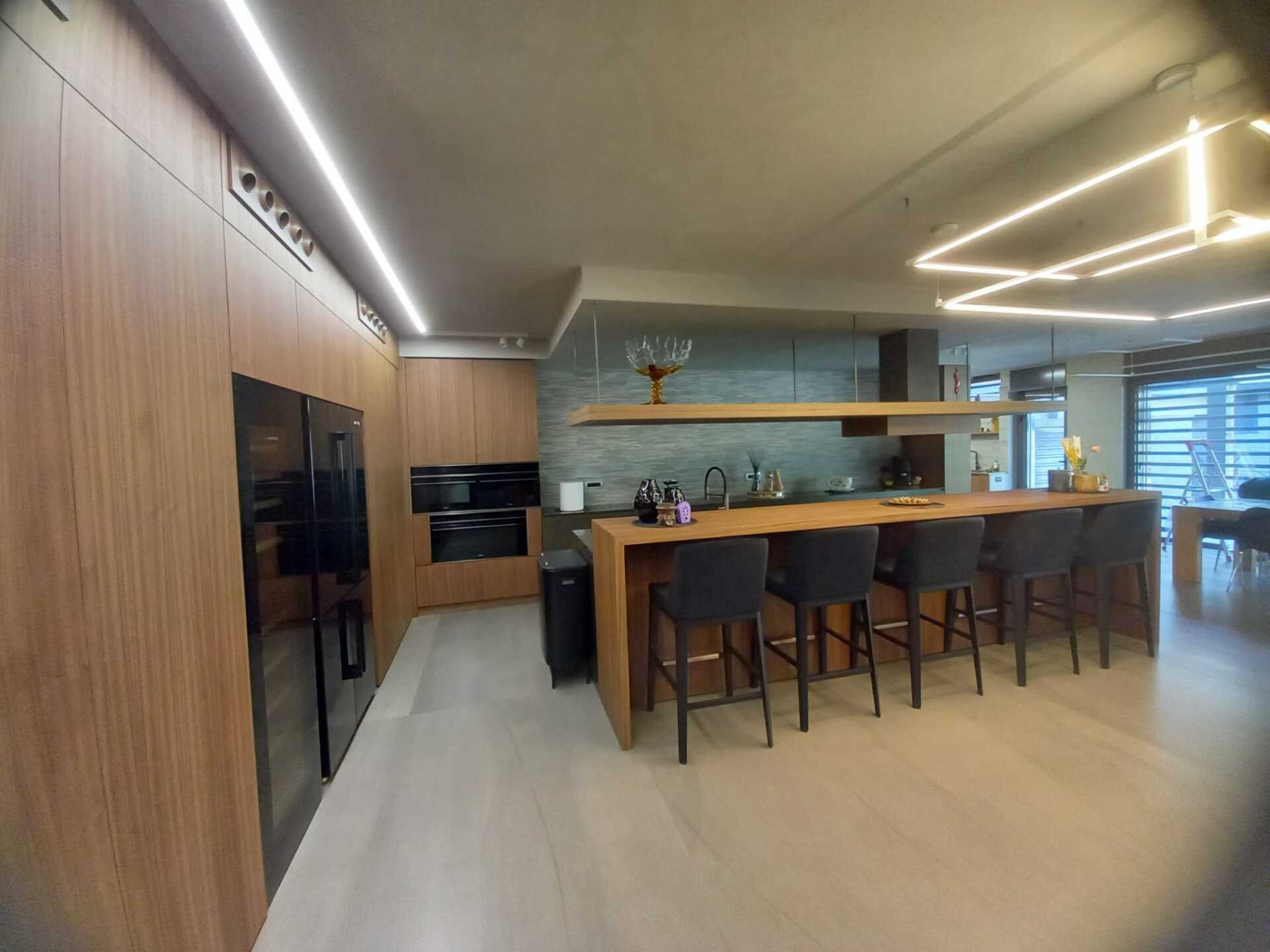 Cucina moderna con mobili in legno, elettrodomestici neri e una lunga isola con sgabelli da bar.