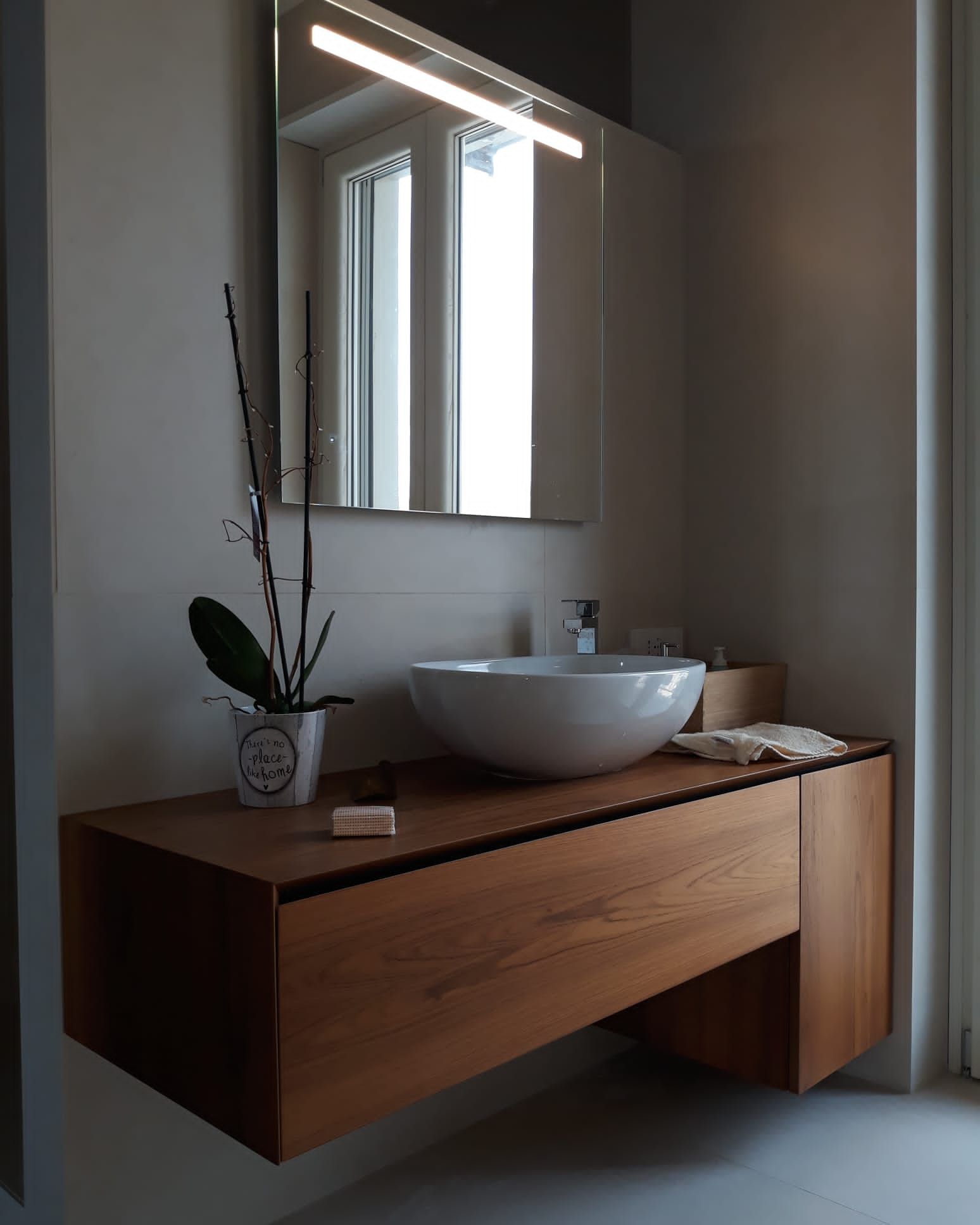 Bagno moderno con mobile lavabo sospeso in legno, lavabo bianco, specchio e orchidea.