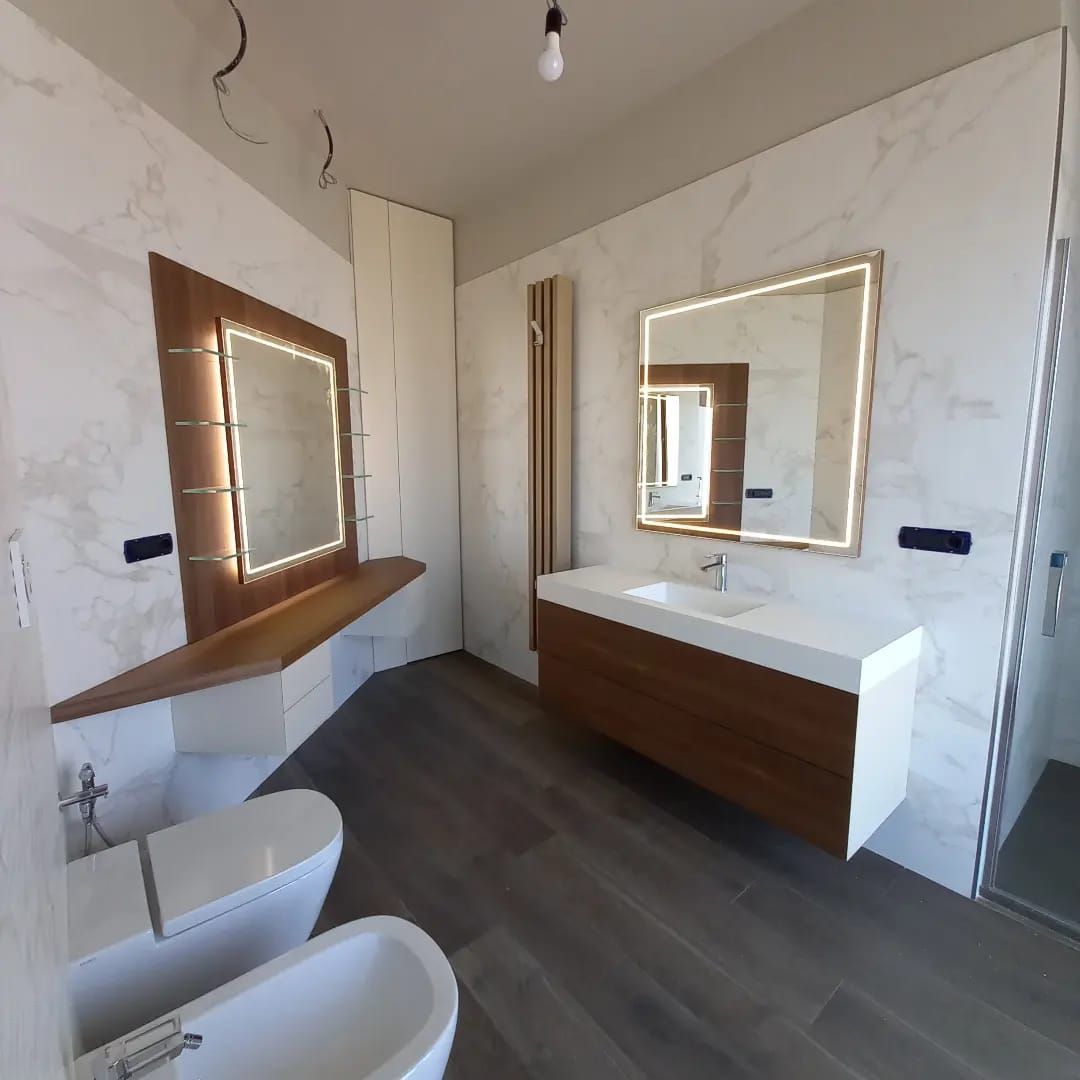 Bagno moderno con pareti in marmo, dettagli in legno e mobile lavabo sospeso.