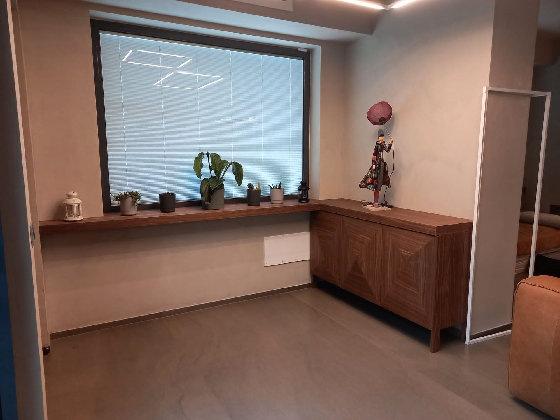 Stanza con finestra, mobiletto in legno e oggetti decorativi su uno scaffale.