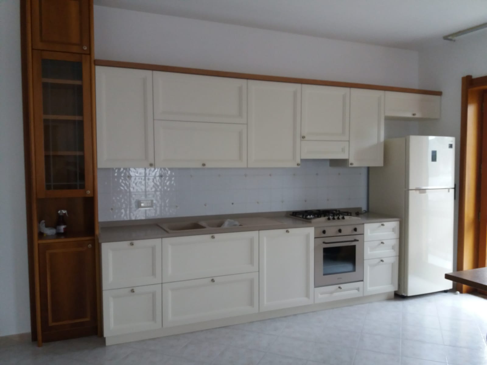 Mobili da cucina color crema con fornello e frigorifero su uno schienale piastrellato bianco.