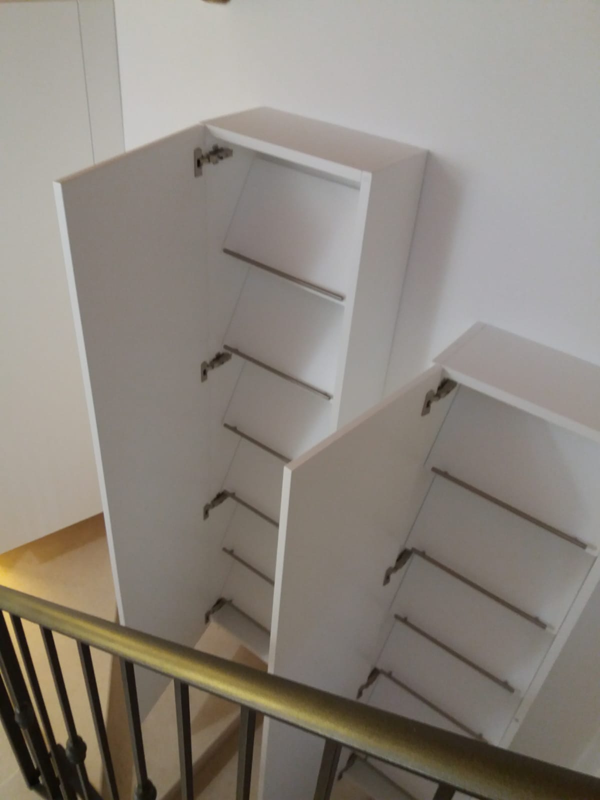 Armadietti bianchi con ante aperte installati sul pianerottolo di una scala, con ripiani in vista.