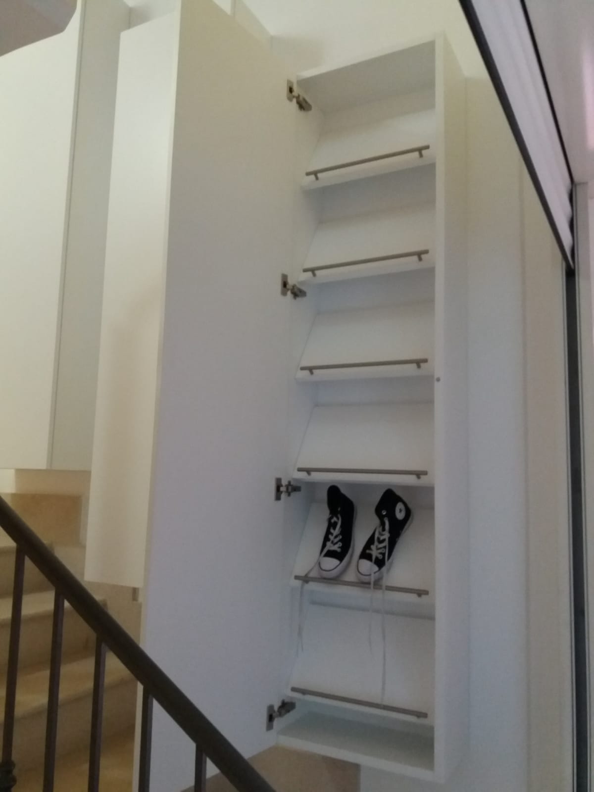 Scarpiera bianca incassata nella parete accanto alla scala, con ripiani angolari per riporre le scarpe.