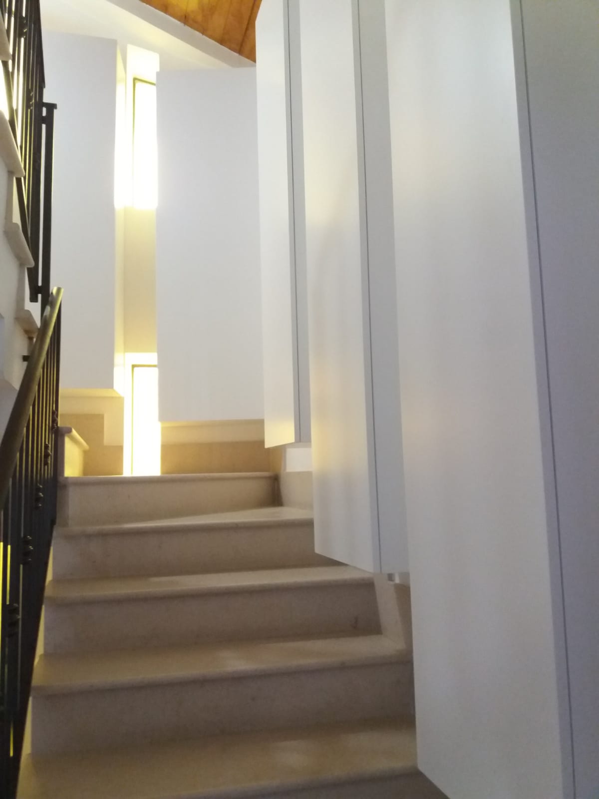 Scala con gradini in pietra e pareti bianche che conduce verso una luminosa finestra rettangolare.