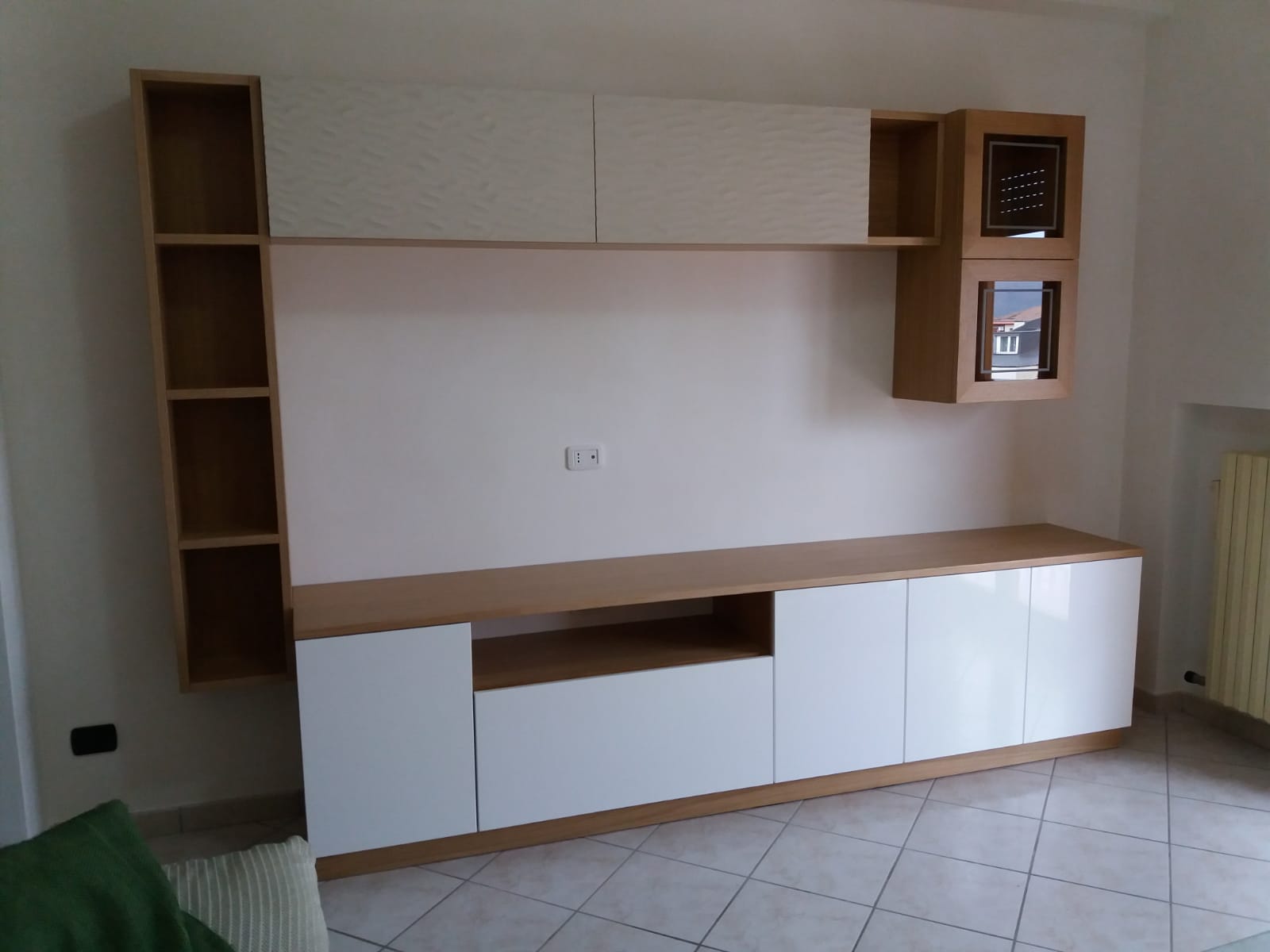 Moderno mobiletto porta TV bianco e legno con mobili contenitori, scaffali e una consolle TV contro una parete bianca.