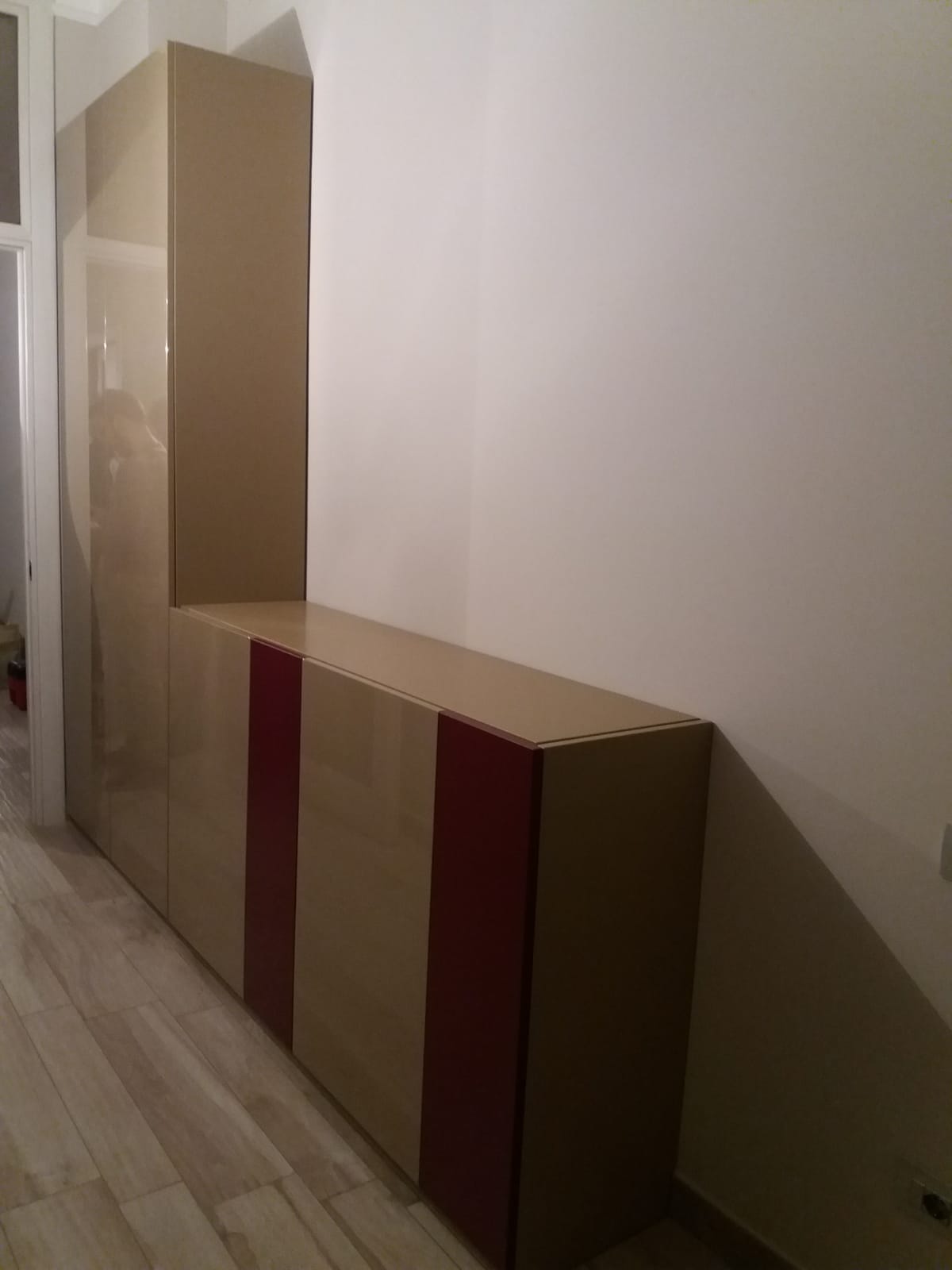 Mobiletto beige e rosso a forma di L contro una parete bianca, in una stanza con pavimento in legno.