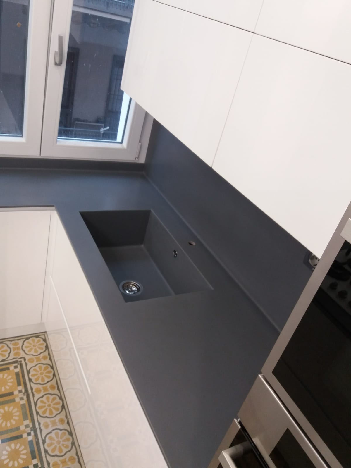 Cucina moderna con piano di lavoro grigio, mobili bianchi e lavello in acciaio inossidabile.