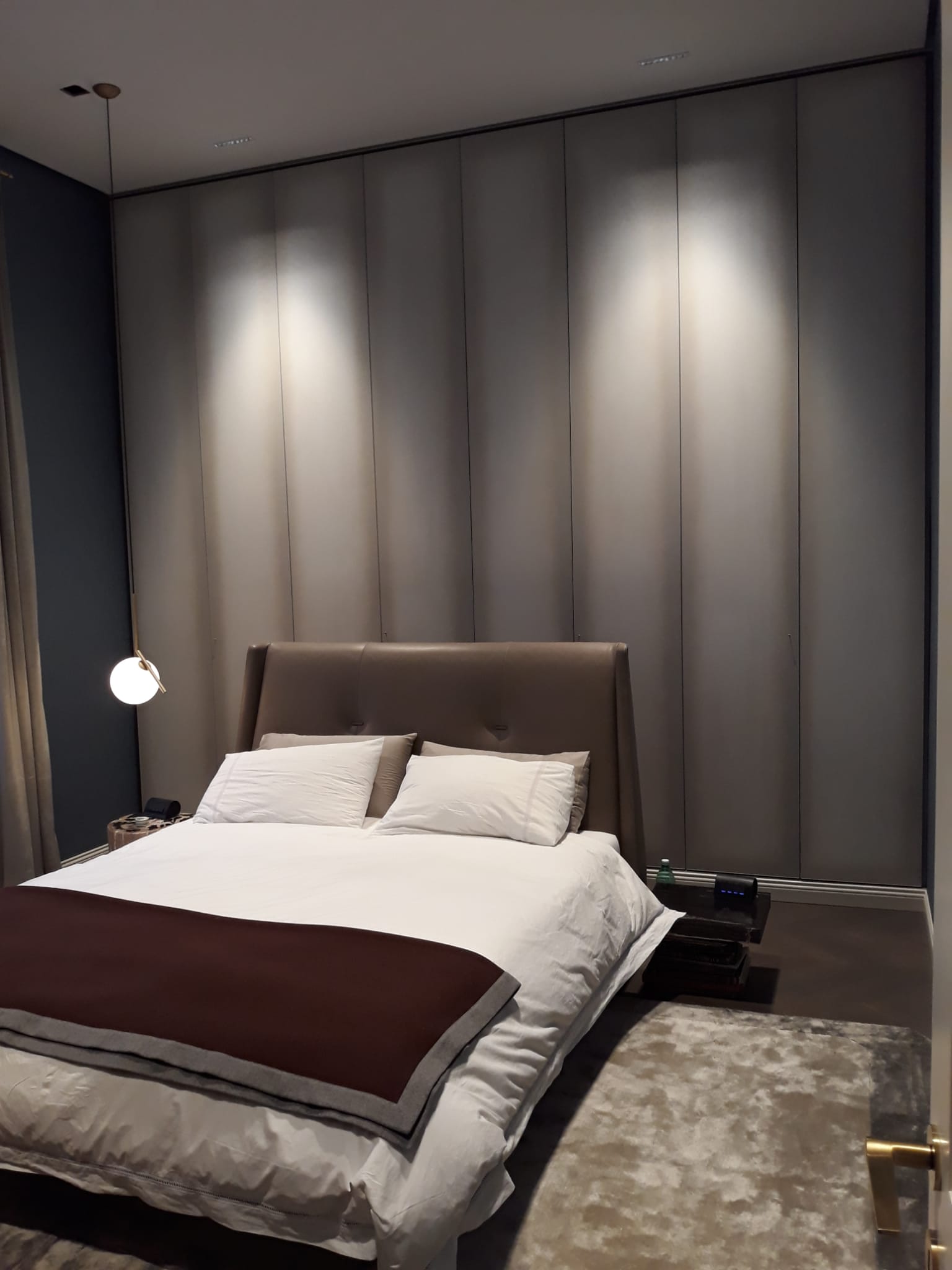 Camera da letto con letto, testiera, parete neutra e illuminazione dall'alto.