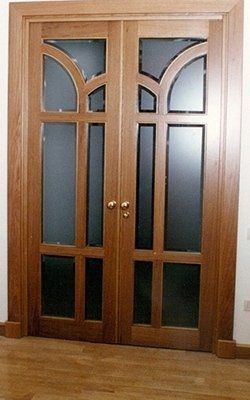 Doppie porte in legno con pannelli in vetro smerigliato e ferramenta dorata, in una stanza con pavimenti in legno.