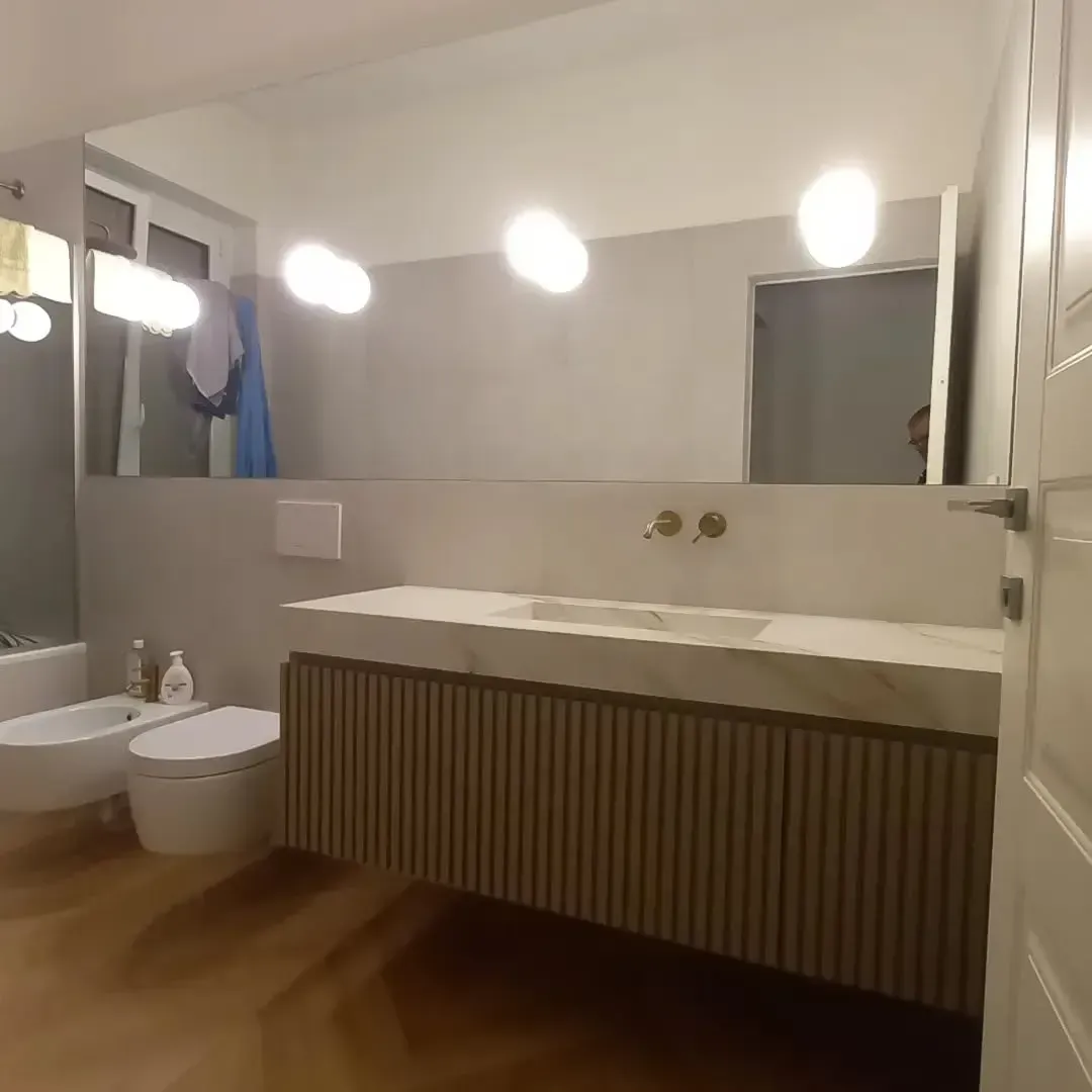 Bagno con ampio specchio, mobile lavabo, WC e bidet. Illuminazione intensa, colori neutri e design moderno.