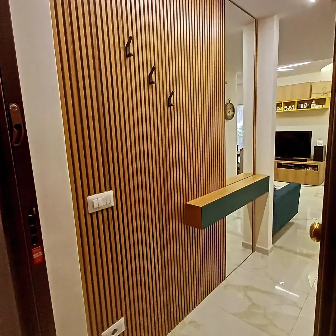 Corridoio con pannelli in legno, ganci appendiabiti, una mensola verde e vista sul soggiorno.