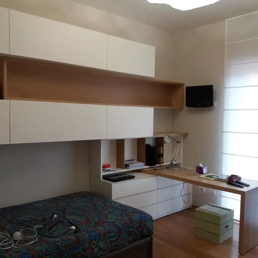 Camera da letto con armadi bianchi a muro, scrivania in legno e un letto con una coperta blu a fantasia.