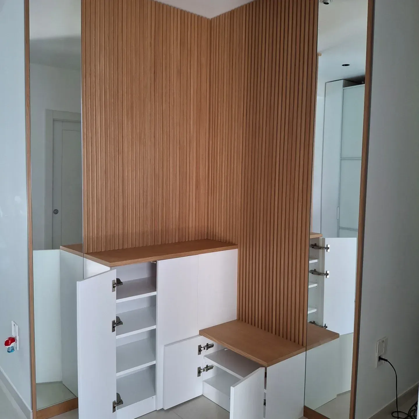 Mobiletto d'ingresso con pannelli in legno e armadi bianchi. Specchi su entrambi i lati dei pannelli.