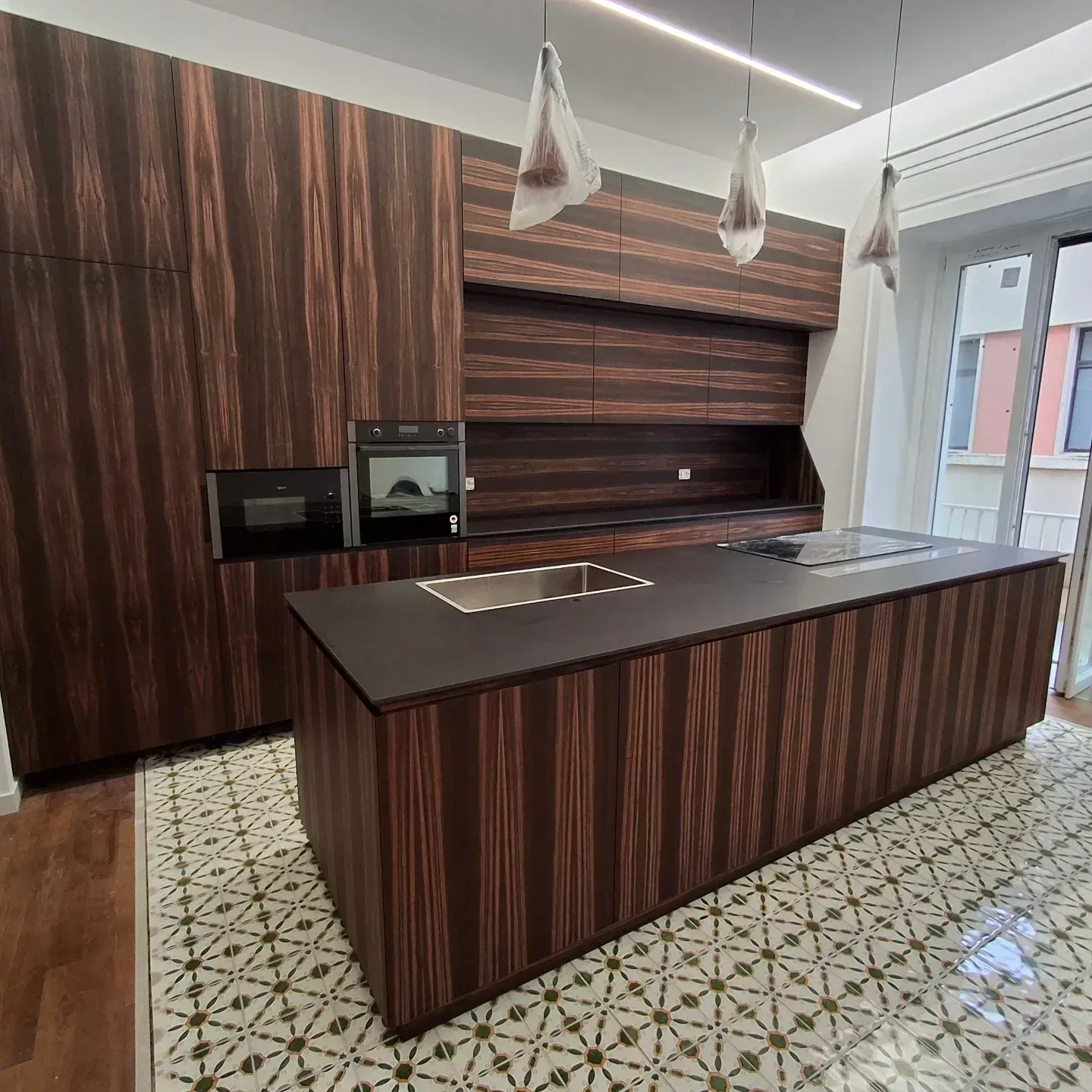 Cucina moderna con mobili in legno, ripiani scuri e pavimento in piastrelle fantasia.